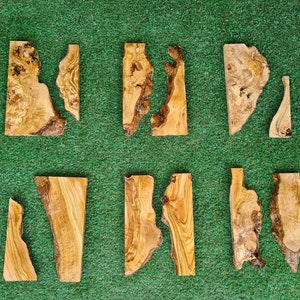 May include: Ten pieces of wood with natural grain patterns and irregular shapes. The wood is light brown with darker brown streaks. The pieces are arranged in two rows of five on a green surface.