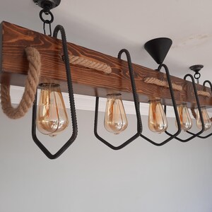 Puede incluir: Una l&aacute;mpara de ara&ntilde;a de madera r&uacute;stica con seis bombillas y un detalle de cuerda. La l&aacute;mpara de ara&ntilde;a tiene una base de madera marr&oacute;n oscura y detalles en metal negro.