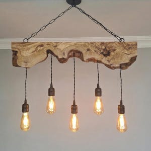 May include: A wooden chandelier with five Edison-style light bulbs. The light fixture is suspended from the ceiling by a black chain and features a natural wood beam with a unique, organic edge. The wood beam is approximately 100 cm in length.