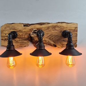 May include: Three black metal industrial style light fixtures with Edison bulbs mounted on a rustic wood plank wall sconce.