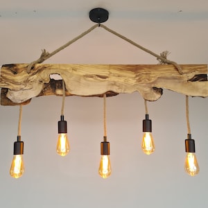 May include: A rustic wooden chandelier with five light bulbs hanging from rope cords. The wood is a natural, light brown color with dark brown knots and grain patterns. The light bulbs are Edison-style with a warm, yellow glow.