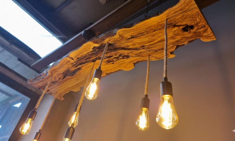Może przedstawiać: Rustykalna lampa wisząca z długą, naturalną deską z widocznym usłojeniem. Pięć żar&oacute;wek w stylu Edisona zwisa z drewna na grubych, teksturowanych sznurach, każda zamocowana w matowej, czarnej metalowej oprawce.