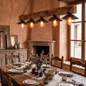 May include: A rectangular wooden beam chandelier with five black metal pendant lights and Edison bulbs, suspended by chains above a long wooden dining table set with ceramic plates, glassware, and a centerpiece of pinecones and foliage.