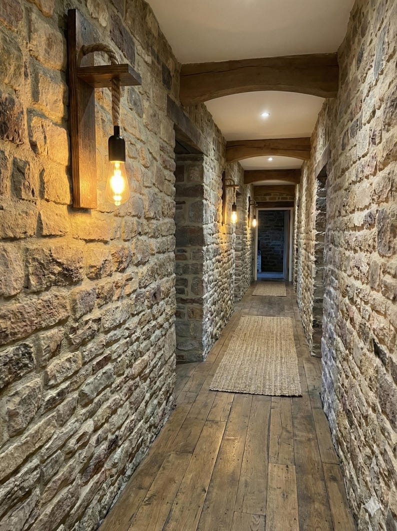 May include: A wall-mounted light fixture featuring a rectangular wooden backplate, a horizontal wooden shelf, and a thick rope cord suspending a black socket with a glowing Edison-style light bulb, installed on a textured stone wall.