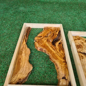 May include: A rectangular wooden frame with a natural wood finish encloses a piece of olive wood with a unique grain pattern. The wood is a light brown color with darker brown streaks. The frame is labeled with the dimensions 20" x 12" and 50 x 30 cm.