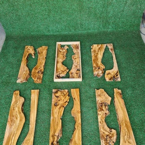 Puede incluir: Un conjunto de ocho piezas de madera con veta de madera natural y nudos. Las piezas son de varios tama&ntilde;os y formas, algunas con un agujero en el centro. La madera es de color marr&oacute;n claro con vetas marrones m&aacute;s oscuras.