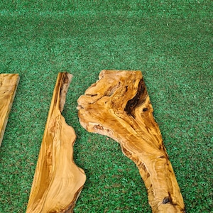 May include: Two pieces of natural wood with a unique grain pattern. The wood is light brown with darker brown streaks. The wood is on a green artificial grass background.
