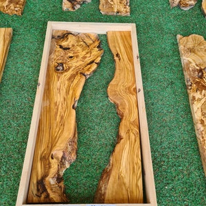 Puede incluir: Una pieza de madera de olivo enmarcada con un relleno de resina natural. La madera tiene un hermoso veteado y es de color marr&oacute;n claro. El marco es de madera natural y es de color marr&oacute;n claro. La pieza mide 24" x 12" o 50 x 30 cm.