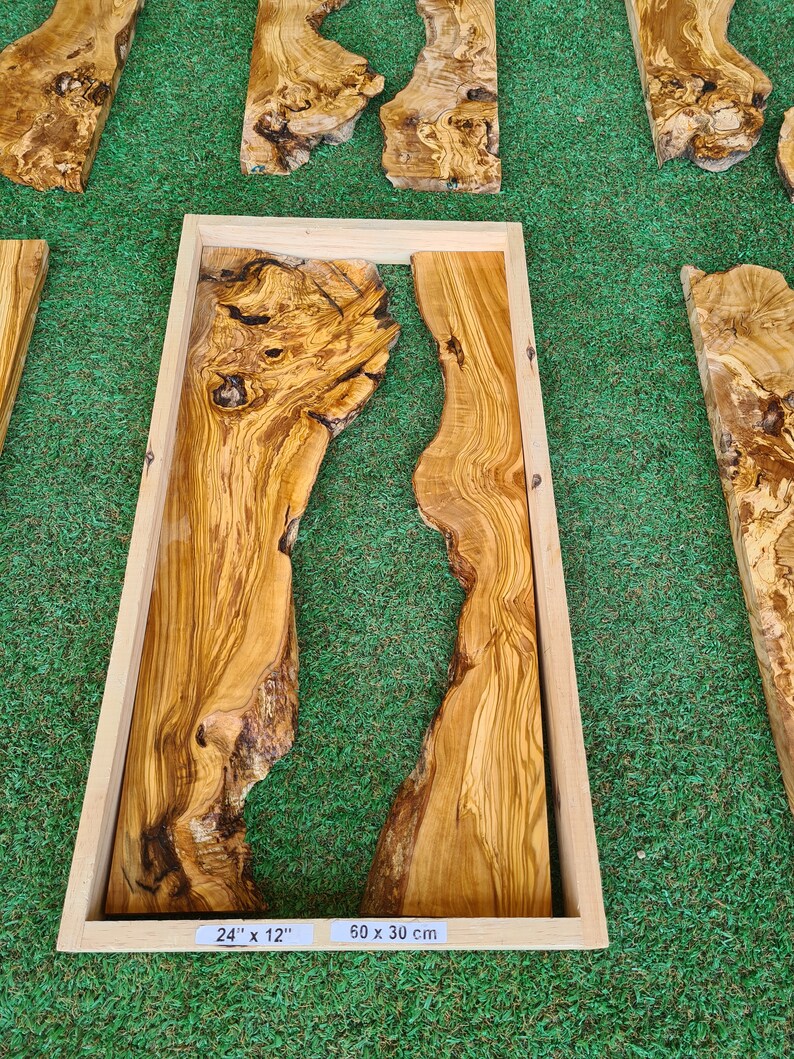 Puede incluir: Una pieza de madera de olivo enmarcada con un relleno de resina natural. La madera tiene un hermoso veteado y es de color marr&oacute;n claro. El marco es de madera natural y es de color marr&oacute;n claro. La pieza mide 24" x 12" o 50 x 30 cm.