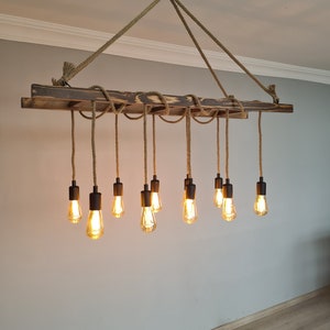 K&ouml;nnte beinhalten: Ein rustikaler Holz-Kronleuchter mit 12 Edison-Gl&uuml;hbirnen, die an Seilschn&uuml;ren h&auml;ngen. Der Kronleuchter ist aus recyceltem Holz gefertigt und hat eine nat&uuml;rliche Oberfl&auml;che.