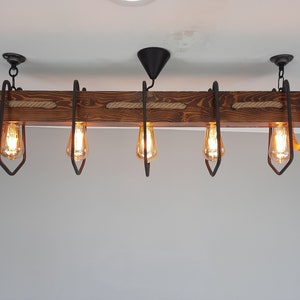 Puede incluir: Una l&aacute;mpara de ara&ntilde;a de madera r&uacute;stica con cinco bombillas y detalles de cuerda. La l&aacute;mpara de ara&ntilde;a est&aacute; hecha de madera oscura y tiene un acabado natural. Las bombillas son de estilo Edison y emiten un brillo c&aacute;lido.