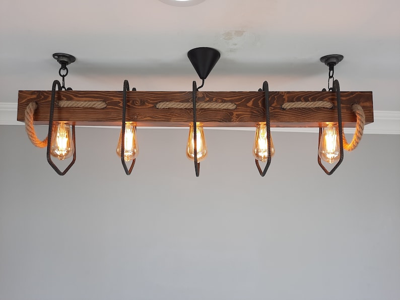 Puede incluir: Una l&aacute;mpara de ara&ntilde;a de madera r&uacute;stica con cinco bombillas y detalles de cuerda. La l&aacute;mpara de ara&ntilde;a est&aacute; hecha de madera oscura y tiene un acabado natural. Las bombillas son de estilo Edison y emiten un brillo c&aacute;lido.