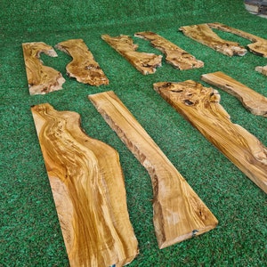 Puede incluir: Una colecci&oacute;n de seis tablas de madera natural con patrones de veta &uacute;nicos y formas diferentes. Las tablas est&aacute;n dispuestas en una fila sobre una superficie de c&eacute;sped artificial verde.