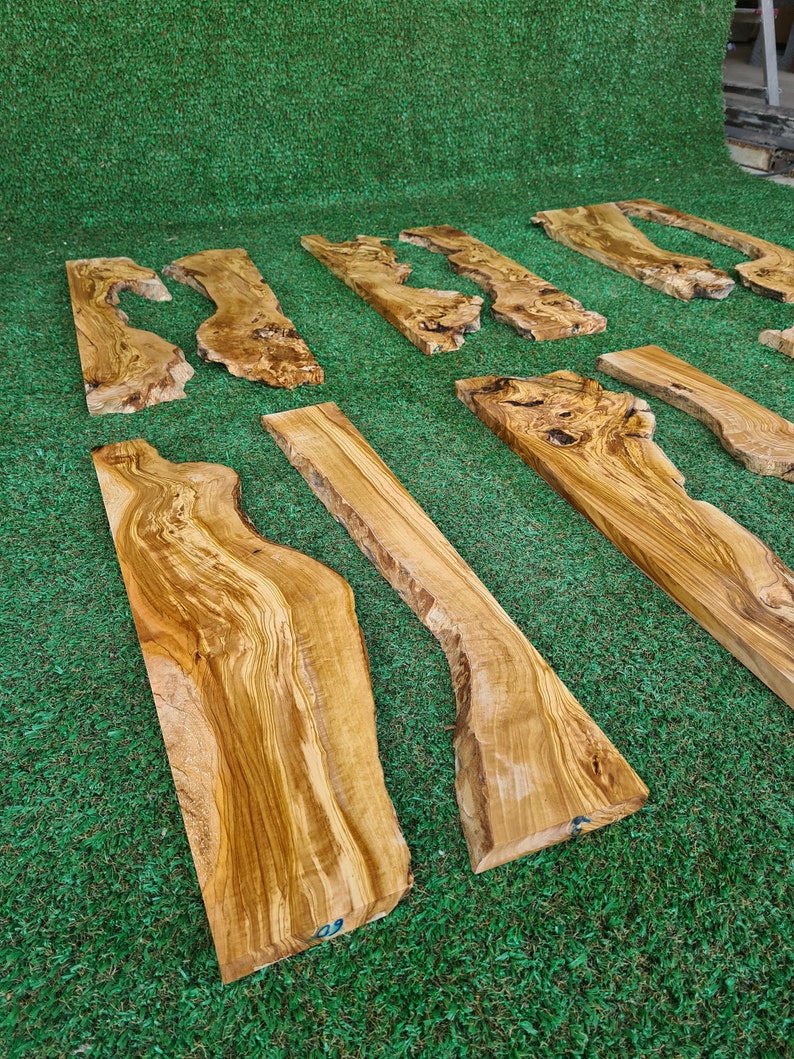 Puede incluir: Una colecci&oacute;n de seis tablas de madera natural con patrones de veta &uacute;nicos y formas diferentes. Las tablas est&aacute;n dispuestas en una fila sobre una superficie de c&eacute;sped artificial verde.