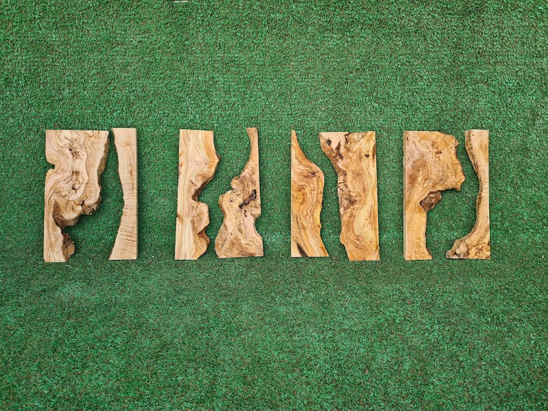May include: Five pieces of wood with natural wood grain and unique shapes. The wood is light brown with darker brown streaks. The pieces are arranged in a row on a green surface.