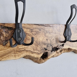 May include: A rustic wall-mounted coat rack featuring a live-edge wooden board with a natural grain pattern. Two black metal hooks are securely attached, providing a functional and stylish storage solution for entryways or bedrooms.