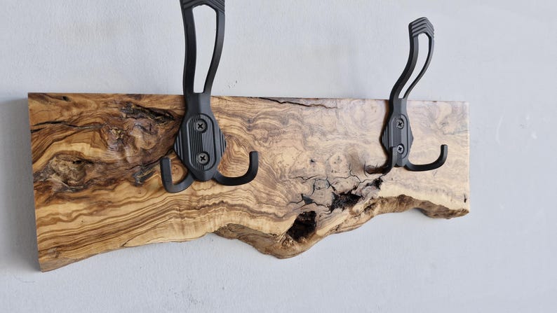 May include: A rustic wall-mounted coat rack featuring a live-edge wooden board with a natural grain pattern. Two black metal hooks are securely attached, providing a functional and stylish storage solution for entryways or bedrooms.