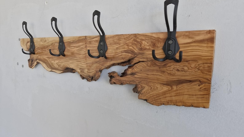 May include: A rustic wooden coat rack with four black metal hooks. The wood has a natural, irregular edge and a warm, brown tone. The hooks are mounted on the wood, creating a functional and decorative piece for entryways or bedrooms.