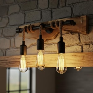 Op de afbeelding: Een rustieke lamp met drie Edison-stijl lampen. De lamp heeft een houten basis, zwarte metalen accenten en touwdetails. De lampen hangen aan de basis en creëren een warme, uitnodigende gloed. De lamp is gemonteerd op een stenen bakstenen muur.