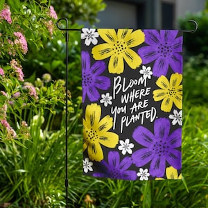 Peut inclure: Un drapeau de jardin rectangulaire avec un fond noir orné de fleurs jaunes et violettes ainsi que de petites fleurs blanches. Le texte "Bloom where you are planted" est imprimé en écriture blanche au centre du drapeau.