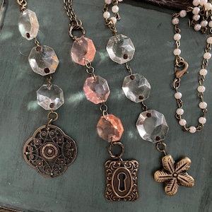 Puede incluir: Tres collares con abalorios de cristal y metal. Los collares presentan cuentas de cristal transparentes y rosadas, un abalorio de ojo de cerradura, un abalorio de flor y un abalorio de filigrana.