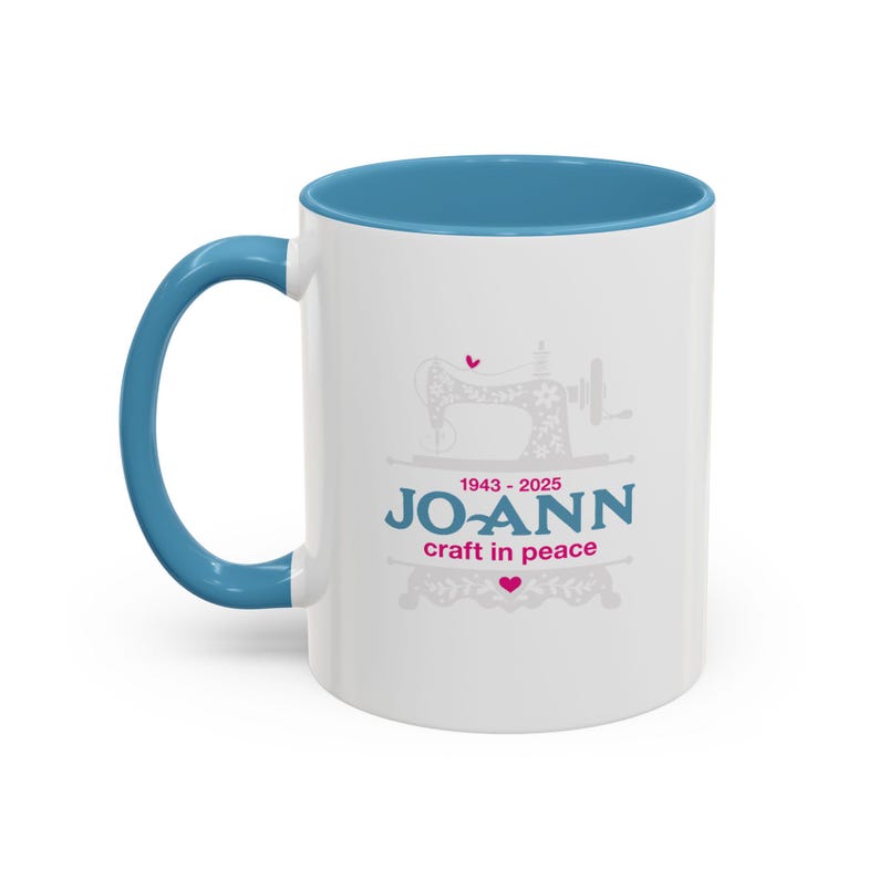 May include: A white ceramic mug with a blue interior and handle. The mug features a gray illustration of a sewing machine and the text "JO-ANN craft in peace" with the years 1943-2025.