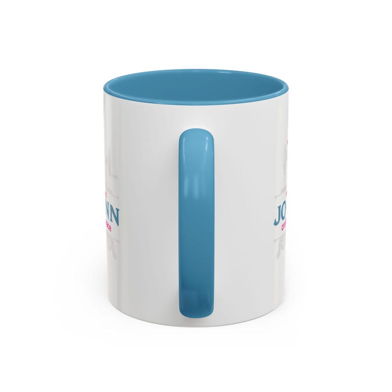 May include: White ceramic mug with a blue interior and handle. The mug features the name "John" in pink and blue text. A decorative floral design is also visible on the mug.