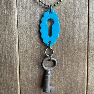 May include: A turquoise blue keyhole charm necklace with a vintage-style key pendant. The keyhole charm has a scalloped edge and the key is made of metal.