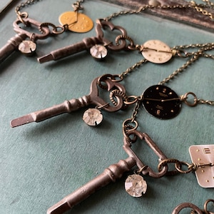 May include: A necklace with three antique keys, each with a crystal charm. The keys are attached to a chain with three vintage watch faces, one gold, one white, and one black.