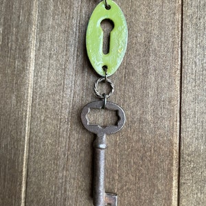 May include: A green keyhole charm with a silver ring attached to a rusty skeleton key.