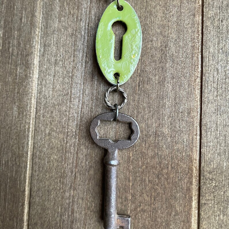 May include: A green keyhole charm with a silver ring attached to a rusty skeleton key.