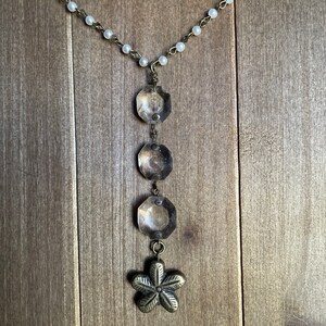 Puede incluir: Un collar de plata con una cadena de perlas blancas y un colgante con cuatro abalorios redondos de plata y un abalorio de flor de plata.