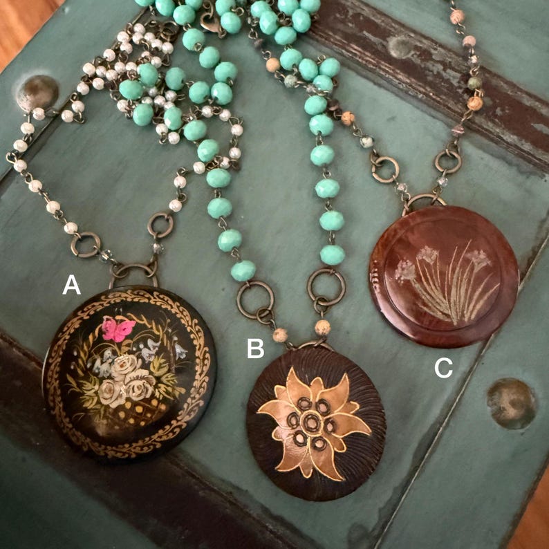 May include: Three necklaces with different pendants. The pendants are round and feature different floral designs. The necklaces are made with turquoise and white beads.
