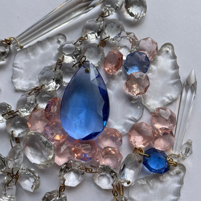 Puede incluir: Una colecci&oacute;n de prismas y l&aacute;grimas de cristal en varios tonos de azul, rosa y transparente. Los cristales est&aacute;n dispuestos en un racimo, con una gran l&aacute;grima azul en el centro.