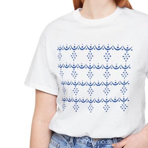 May include: White t-shirt with a blue geometric pattern of snowflakes and curved lines. The pattern is repeated across the shirt.