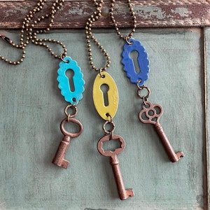 May include: Three keyhole-shaped pendants on gold chains with antique keys attached. The pendants are painted in shades of blue, yellow, and green.