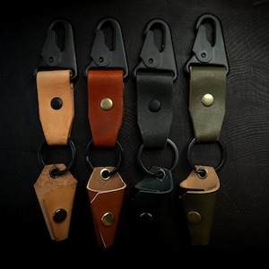 May include: Four leather keychains with black metal clips and key rings. The keychains are in different colors: tan, brown, black, and green.