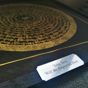 Puede incluir: Un mandala negro y dorado enmarcado con detalles intrincados. El marco tiene una placa plateada con el texto "Your Text Will Be Engraved Here".