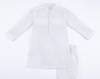 Puede incluir: Un conjunto blanco de dos piezas para niños. La parte superior de manga larga presenta un cuello mandarín y bordados decorativos en el pecho. Los pantalones a juego tienen cintura elástica. El conjunto está hecho de tela ligera.