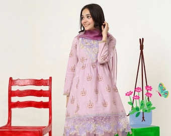 Puede incluir: Un conjunto de dos piezas de color lila claro con una parte superior de manga larga y pantalones a juego. La parte superior presenta bordados dorados y morados y un diseño floral. Una silla roja y un bloque verde están en el fondo.