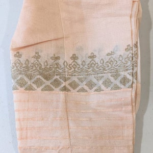 May include: Peach-colored fabric with gold decorative borders. The fabric has a textured appearance with horizontal lines and ornate patterns. The borders feature geometric and floral designs, adding a touch of elegance to the textile.