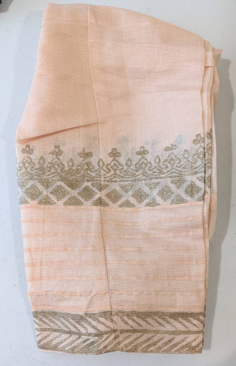 May include: Peach-colored fabric with gold decorative borders. The fabric has a textured appearance with horizontal lines and ornate patterns. The borders feature geometric and floral designs, adding a touch of elegance to the textile.