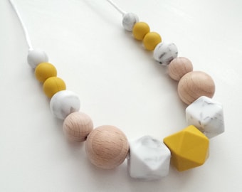 May include: A yellow and white silicone and wood bead necklace. The necklace features a variety of shapes and sizes of beads, including round, square, and rectangular beads.