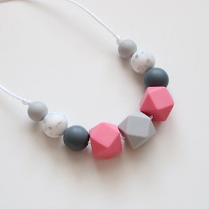 May include: A necklace made of silicone beads in shades of gray and pink. The beads are round and geometric, with a white marbled bead included.