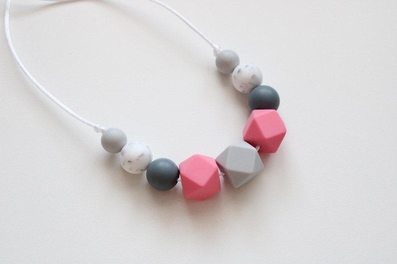 May include: A necklace made of silicone beads in shades of gray and pink. The beads are round and geometric, with a white marbled bead included.