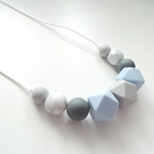 May include: A gray, white, and light blue silicone necklace with geometric and round beads.