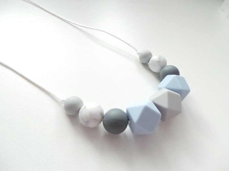 May include: A gray, white, and light blue silicone necklace with geometric and round beads.