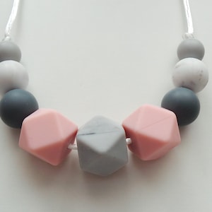 May include: A necklace made of silicone beads in shades of gray and pink. The beads are in a variety of shapes, including round, square, and hexagonal.