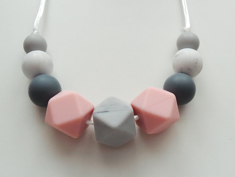 May include: A necklace made of silicone beads in shades of gray and pink. The beads are in a variety of shapes, including round, square, and hexagonal.