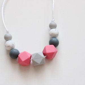 May include: A pink and gray silicone necklace with geometric beads. The necklace is made of a soft, flexible material and is perfect for teething babies.